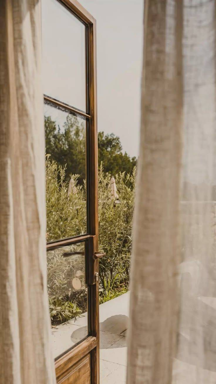 Linen curtains drawn back from an open window onto a garden