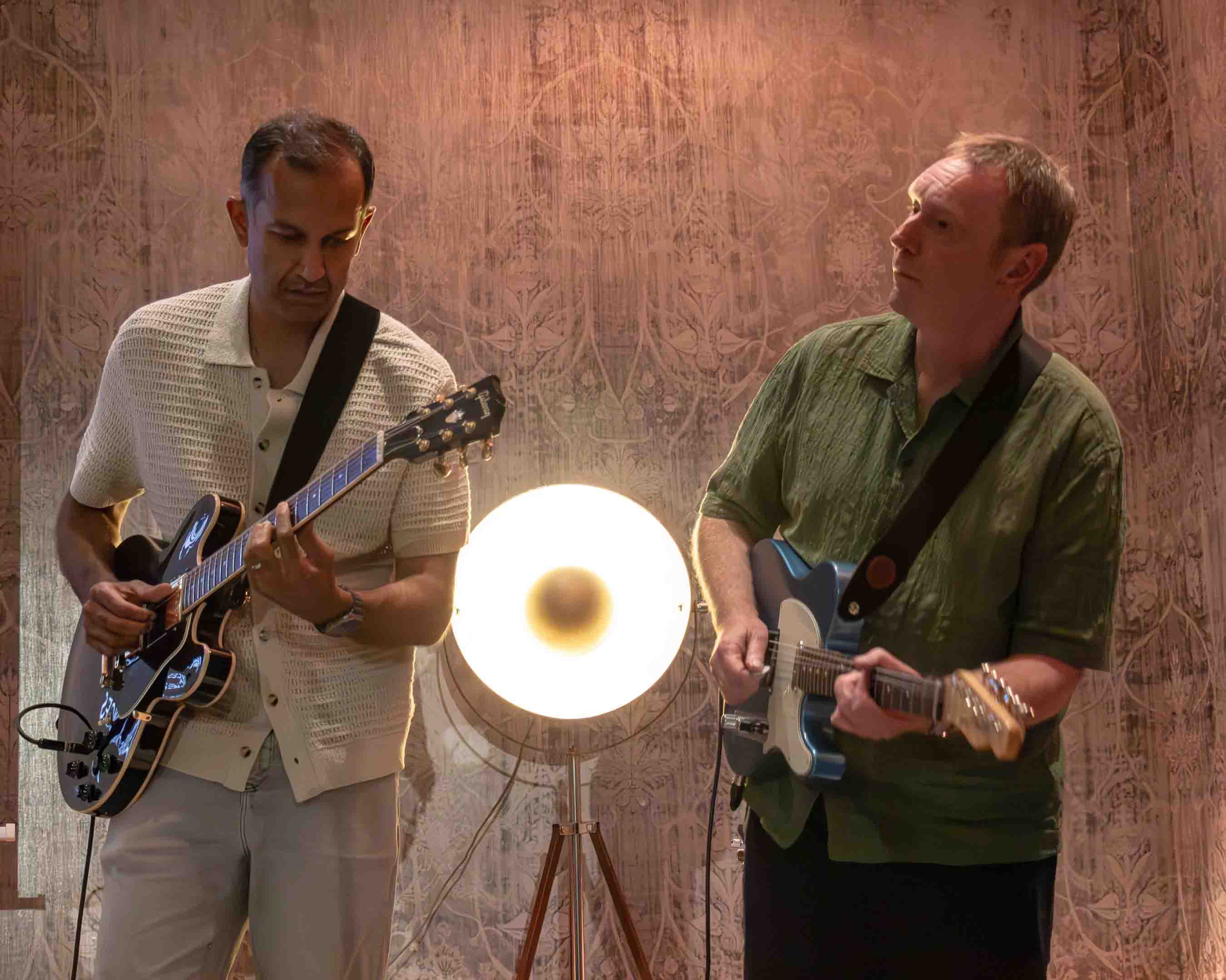Two guitarists playing together beside a lamp during an evening jam
