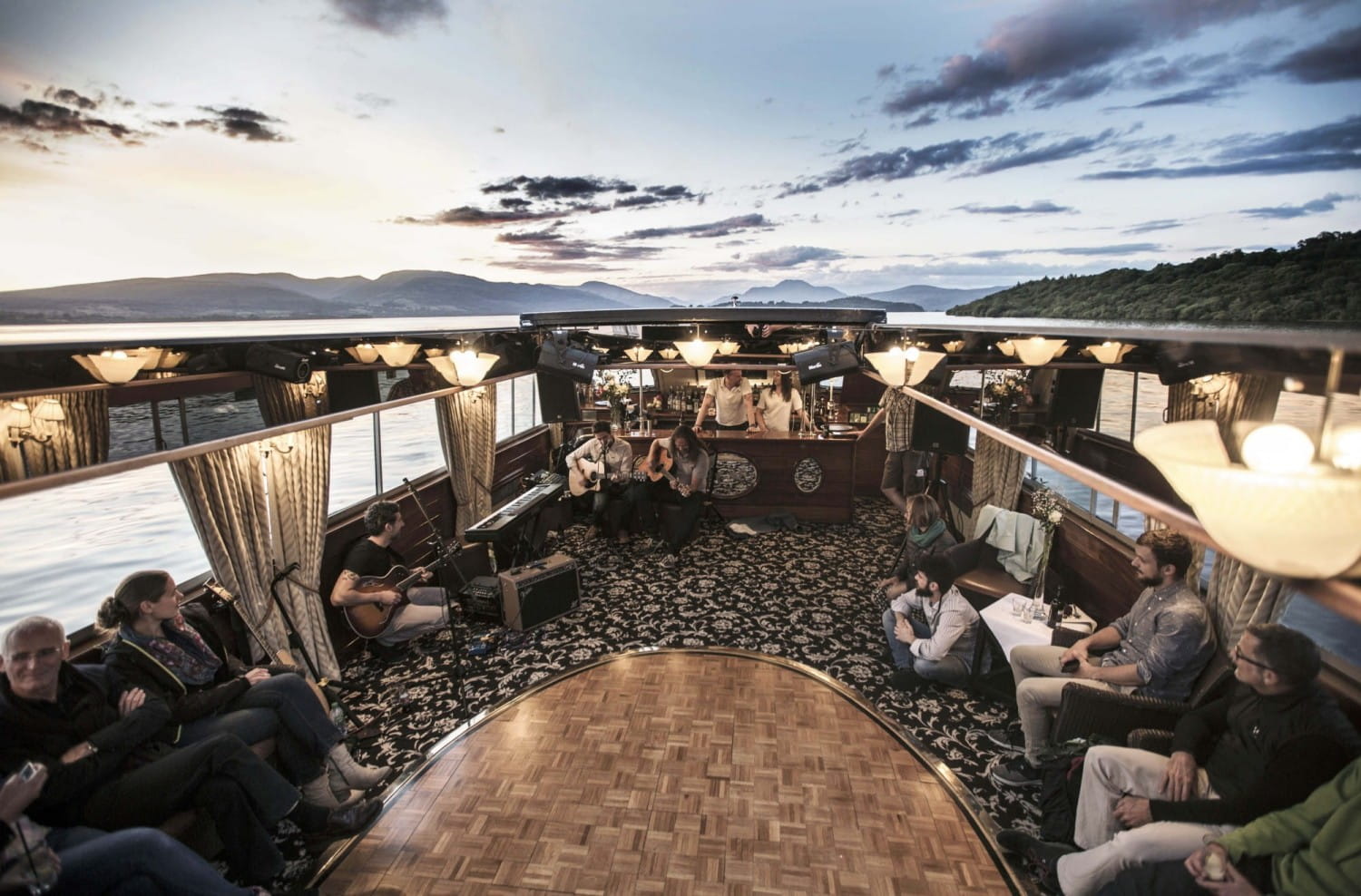 Guests on the deck of a cruise boat on Loch Lomond at sunset