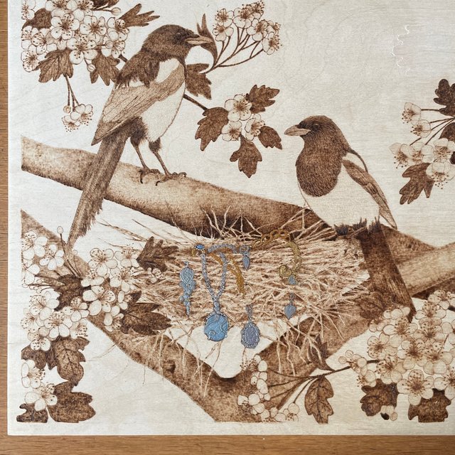 Two magpies and a nest burned onto a flat wood panel