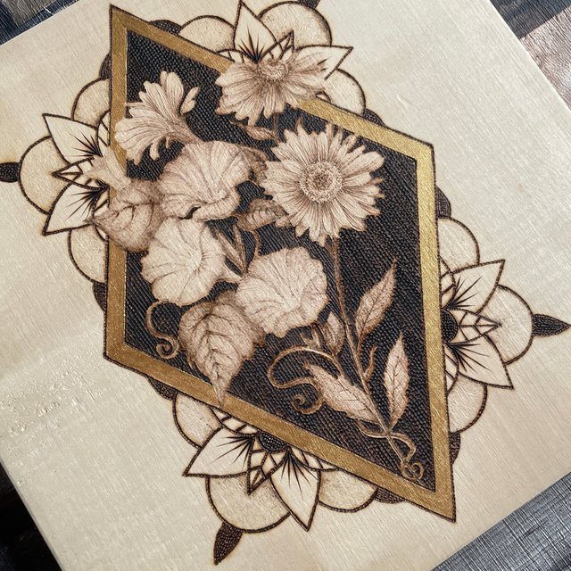 A gold-framed floral piece on pale, clean-grained wood