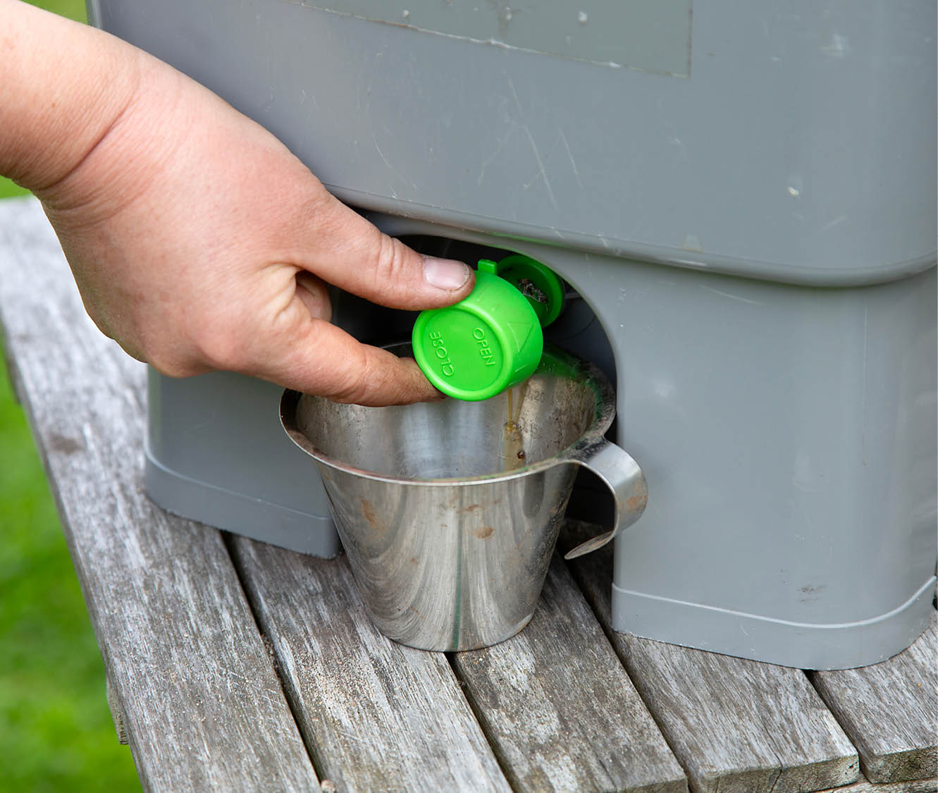 Hand opening green tap on grey compost bin with metal collection bucket below