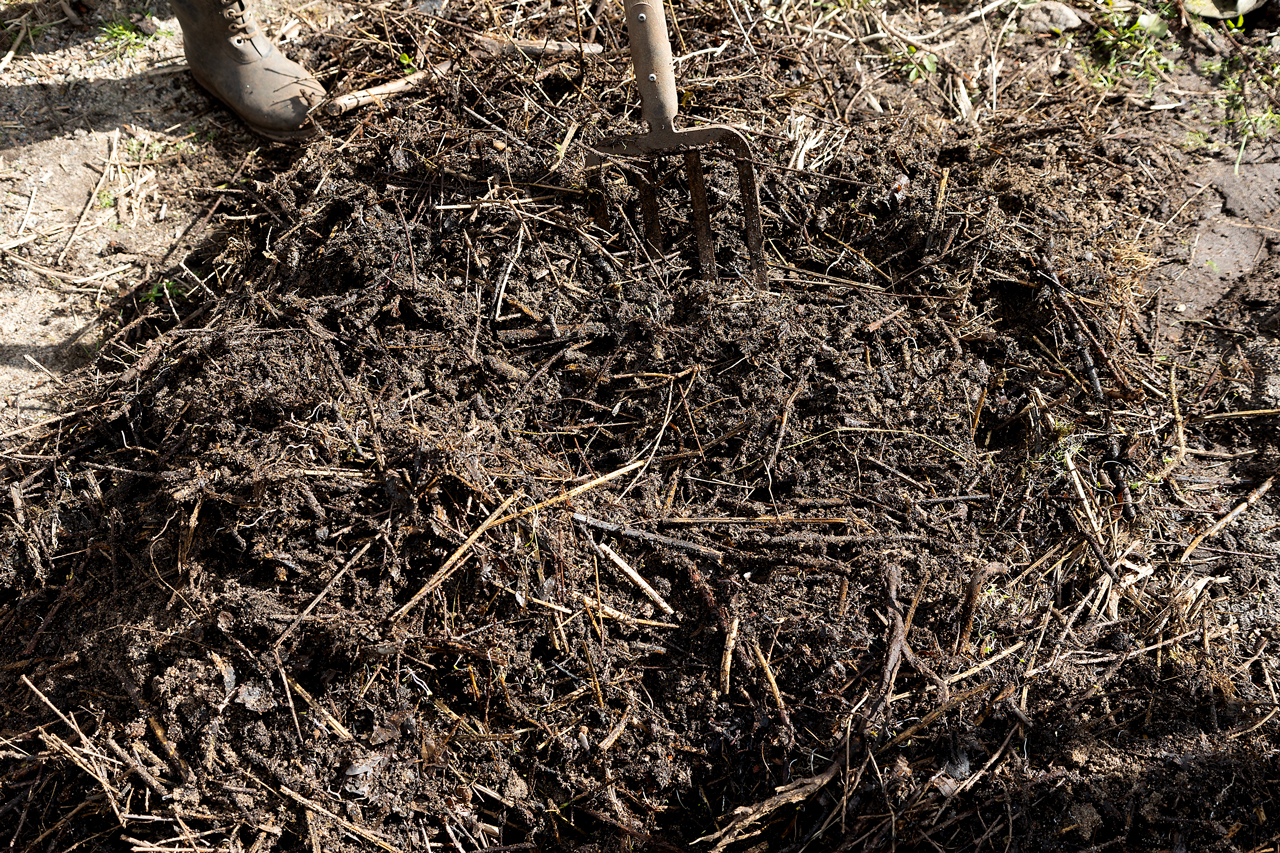 Person using fork to turn soil and compost with straw and organic matter