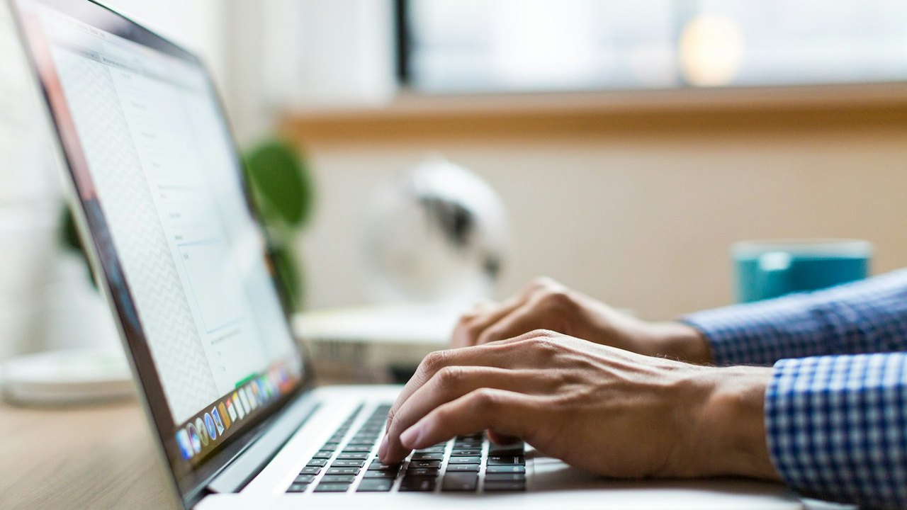 Hands typing on a laptop at a wooden desk in daylight