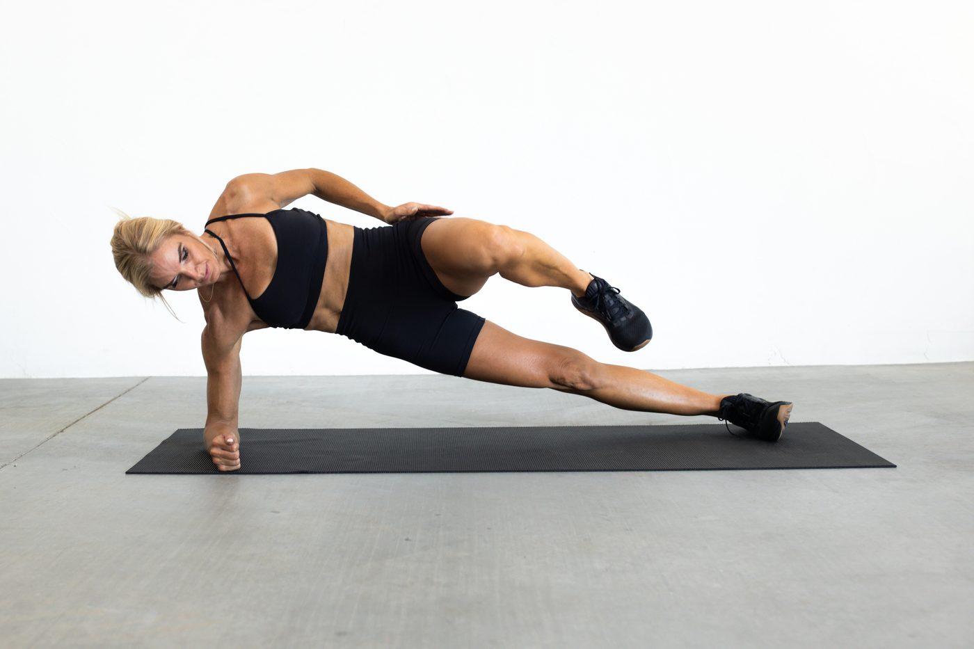 Andrea holding a side plank with knee drive on a mat