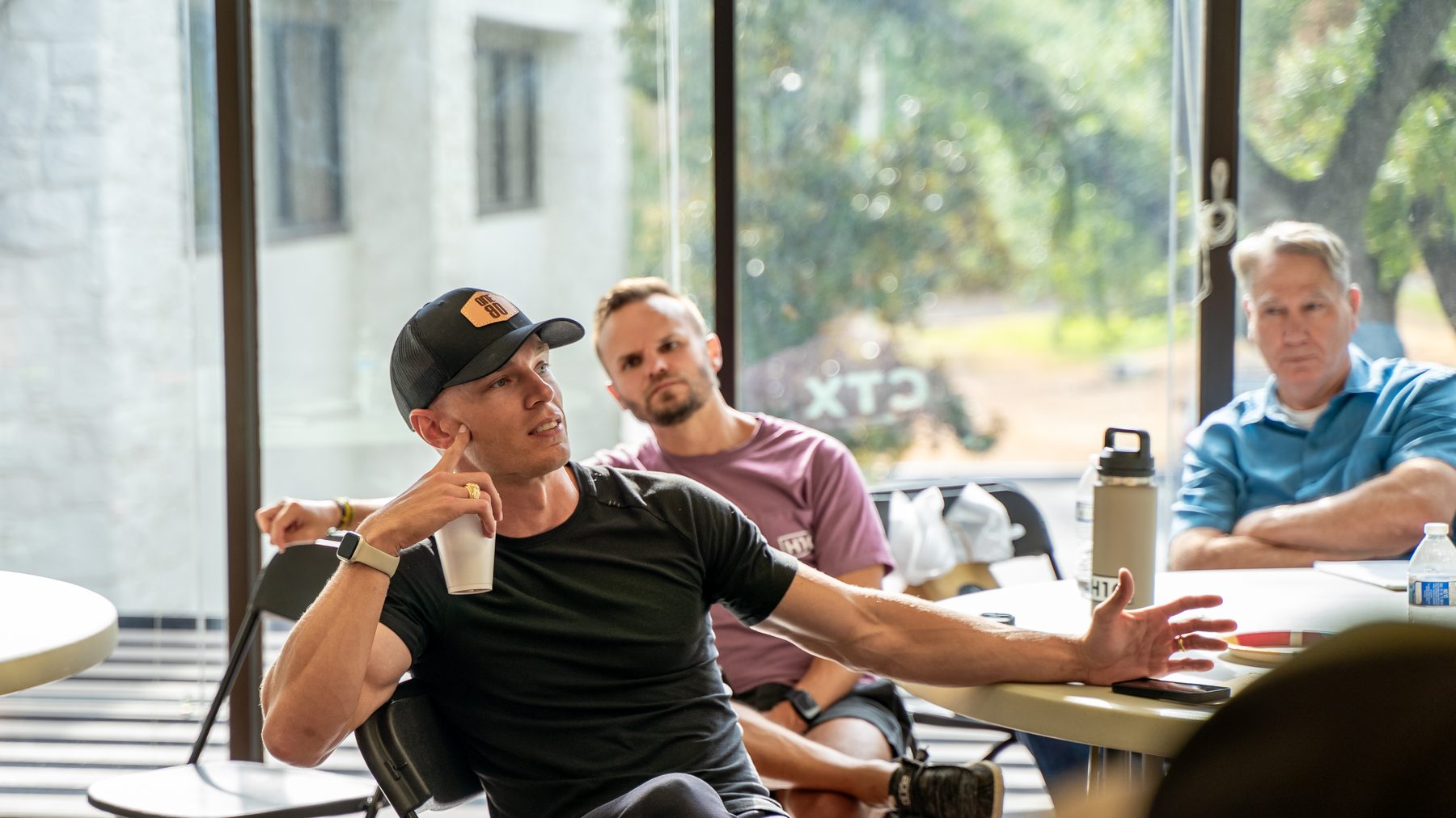 A ministry leader mid-sentence at a table, talking things through with two others listening.