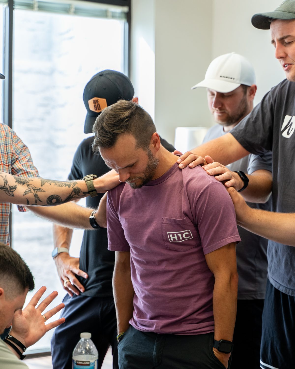 A ministry leader with his head bowed while others lay hands on his shoulders and pray over him.