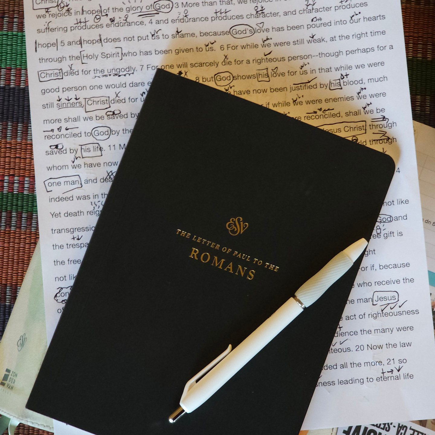 A journal and pen resting on marked-up notes from Romans