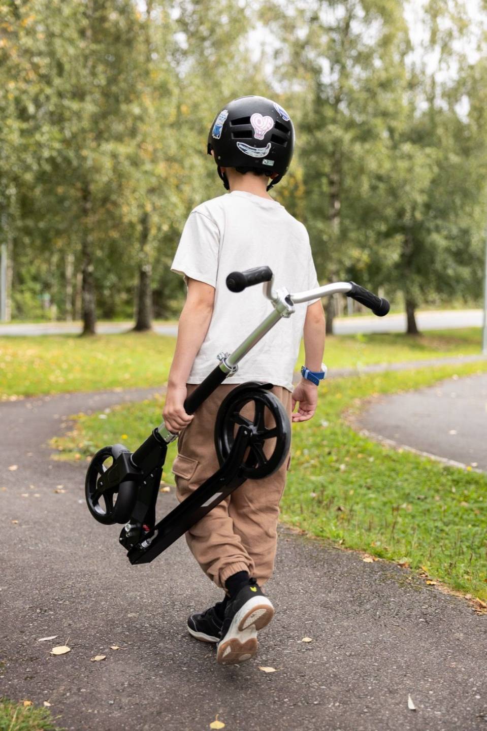 Et barn bærer sparkesykkelen langs en sti ute, livsstilsbilde.